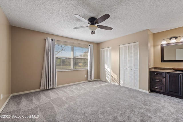 unfurnished bedroom with multiple closets, light colored carpet, ceiling fan, and a textured ceiling