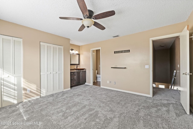 unfurnished bedroom with ensuite bathroom, carpet floors, two closets, and a textured ceiling