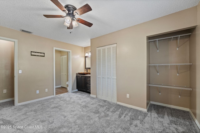 unfurnished bedroom with two closets, ensuite bath, carpet flooring, ceiling fan, and a textured ceiling