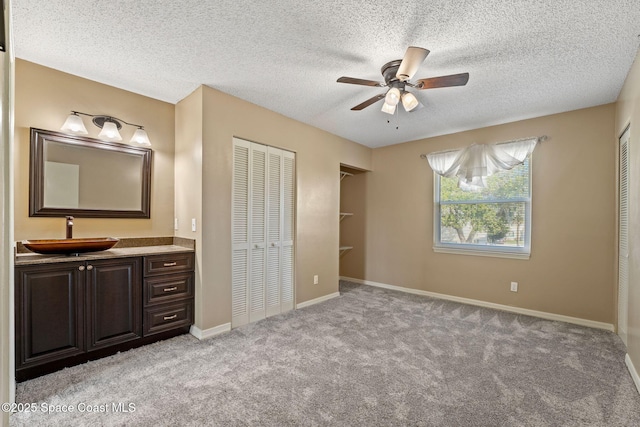 unfurnished bedroom featuring sink, ceiling fan, a textured ceiling, light carpet, and a closet