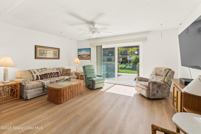 living room featuring ceiling fan, light hardwood / wood-style flooring, and a textured ceiling