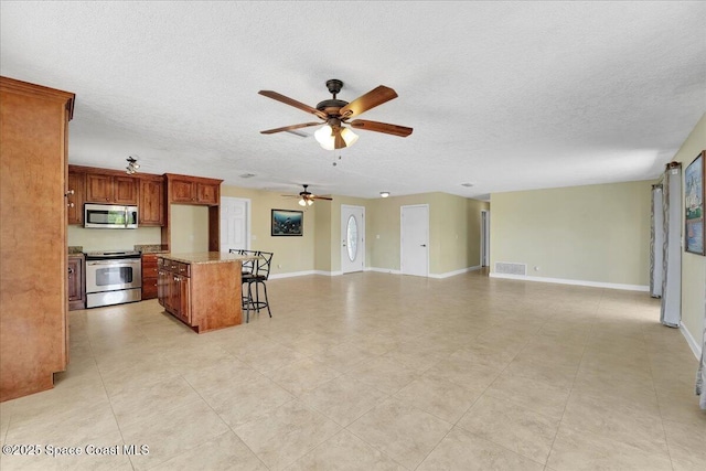 kitchen featuring ceiling fan, a center island, a kitchen breakfast bar, a textured ceiling, and appliances with stainless steel finishes