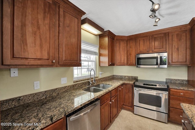 kitchen featuring sink, dark stone countertops, track lighting, light tile patterned floors, and appliances with stainless steel finishes