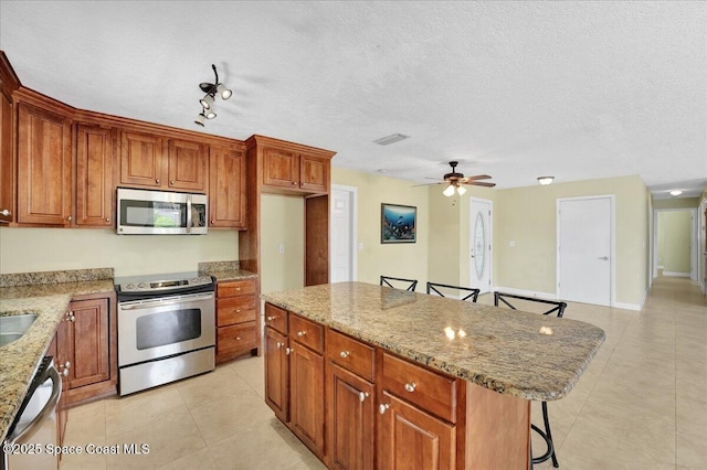 kitchen with a center island, ceiling fan, light stone counters, appliances with stainless steel finishes, and a kitchen bar