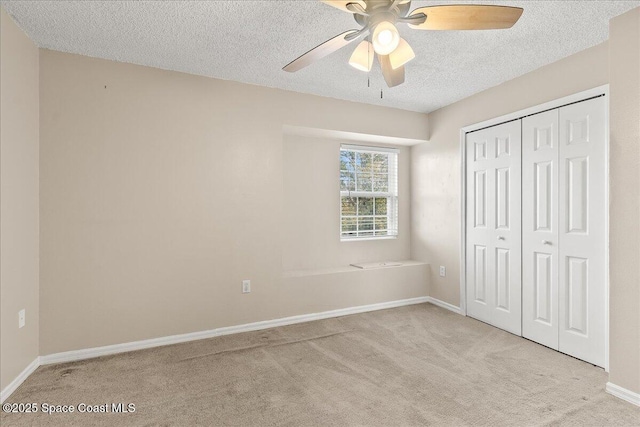 unfurnished bedroom with ceiling fan, a closet, light colored carpet, and a textured ceiling