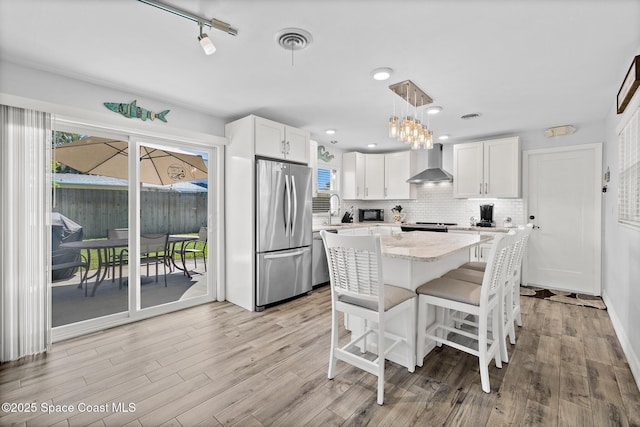 346 Cyprus Dr, Cocoa Beach, FL 32931 - kitchen featuring stainless steel appliances, wall chimney range hood, white cabinetry, and light wood finished floors