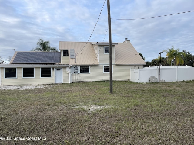 rear view of property featuring solar panels and a lawn