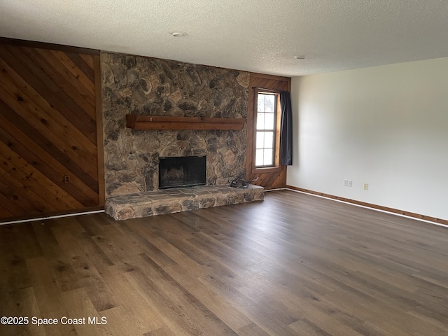 unfurnished living room featuring a textured ceiling, dark hardwood / wood-style floors, a stone fireplace, and wooden walls