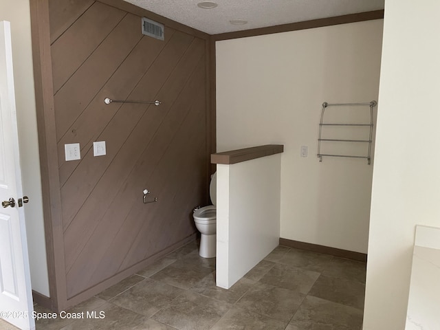 bathroom featuring wood walls, toilet, and a textured ceiling