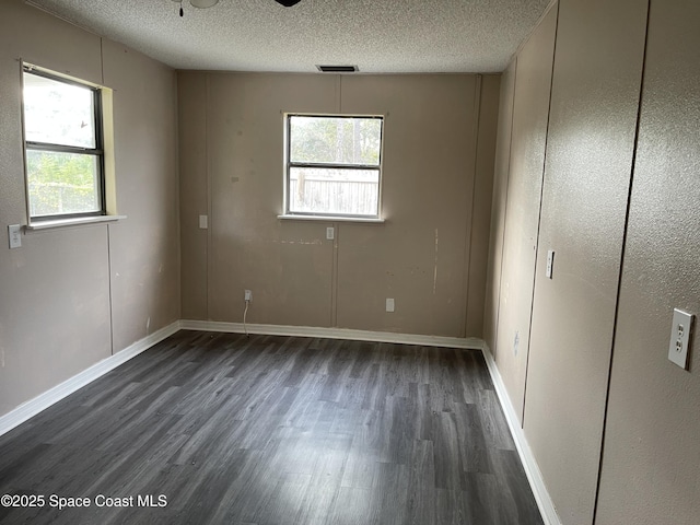 spare room featuring a textured ceiling, a healthy amount of sunlight, and dark hardwood / wood-style floors