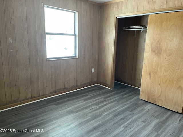 unfurnished bedroom featuring dark hardwood / wood-style flooring, a closet, and wooden walls