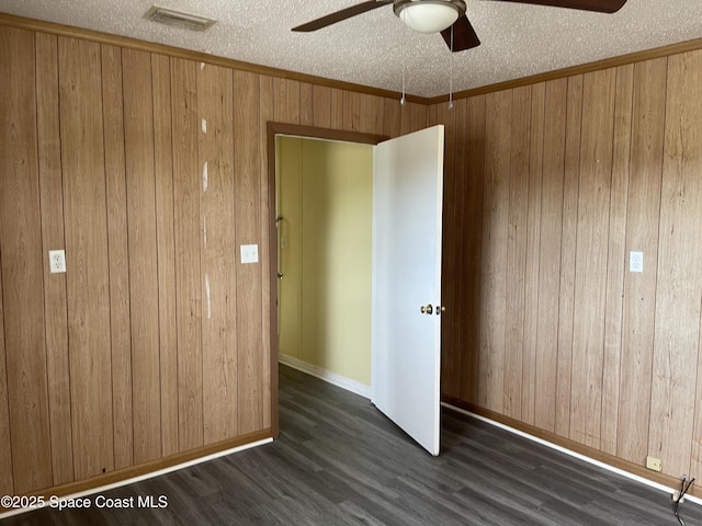 unfurnished bedroom with a textured ceiling, ceiling fan, crown molding, dark hardwood / wood-style floors, and wood walls