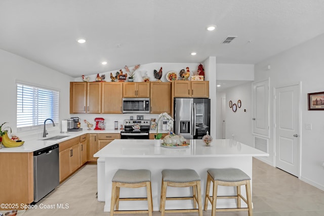 kitchen with sink, light tile patterned floors, appliances with stainless steel finishes, a kitchen island, and a kitchen bar