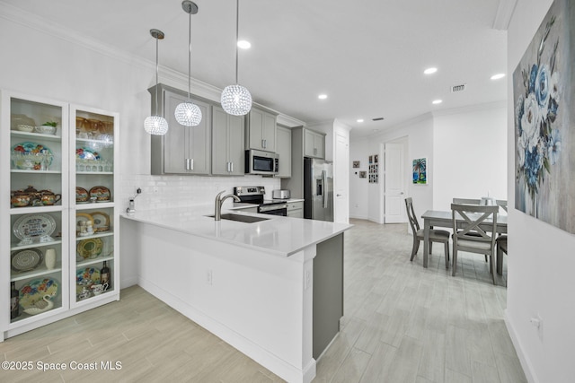 kitchen featuring kitchen peninsula, appliances with stainless steel finishes, gray cabinetry, sink, and pendant lighting