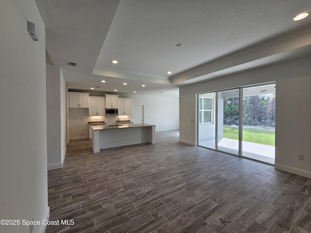 kitchen with white cabinetry, a kitchen island with sink, dark hardwood / wood-style floors, and a raised ceiling