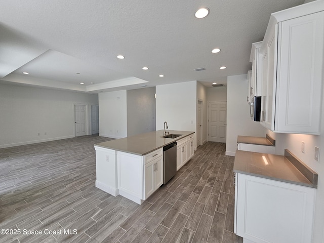 kitchen with dishwasher, white cabinets, a tray ceiling, sink, and a kitchen island with sink