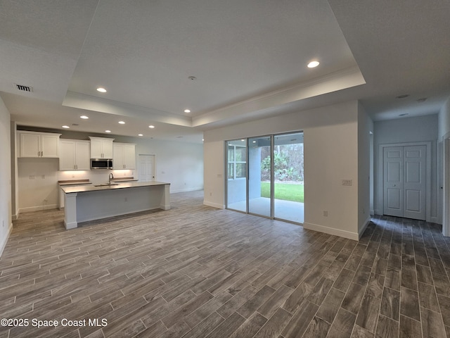 kitchen featuring white cabinets, an island with sink, a tray ceiling, and sink