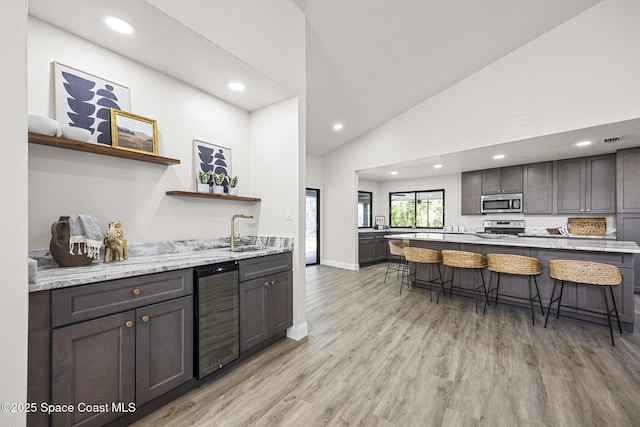 kitchen featuring sink, stainless steel appliances, wine cooler, high vaulted ceiling, and a breakfast bar