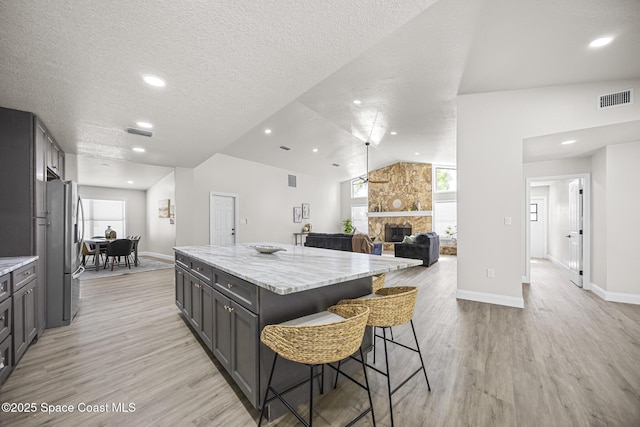 kitchen with light stone counters, light hardwood / wood-style flooring, lofted ceiling, a kitchen island, and a stone fireplace