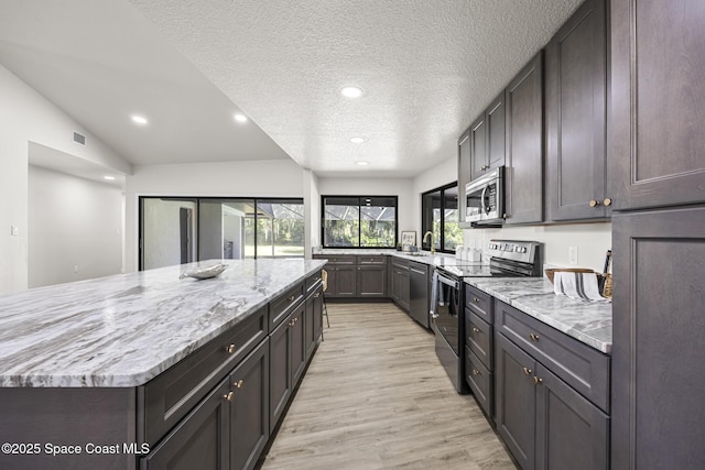 kitchen with sink, light stone counters, a textured ceiling, appliances with stainless steel finishes, and light wood-type flooring