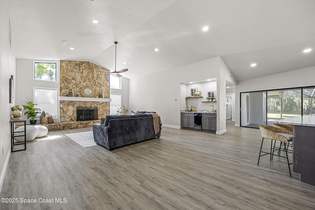 living room with a stone fireplace, high vaulted ceiling, a textured ceiling, and hardwood / wood-style flooring