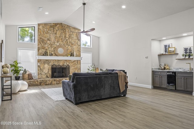 living room featuring a fireplace, high vaulted ceiling, light hardwood / wood-style flooring, and wine cooler