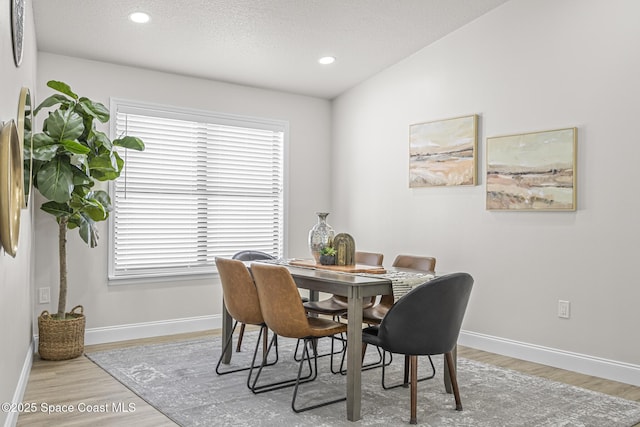 dining space with a textured ceiling, light hardwood / wood-style floors, and vaulted ceiling