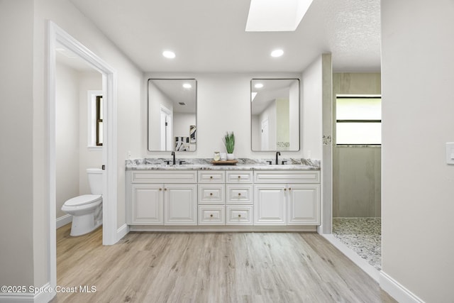 bathroom with a skylight, a shower, wood-type flooring, toilet, and vanity