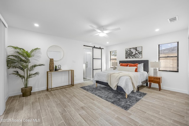 bedroom with a barn door, ceiling fan, and light hardwood / wood-style flooring