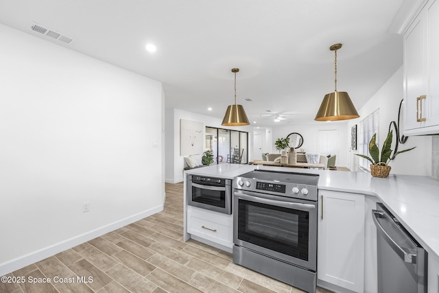 kitchen featuring white cabinets, pendant lighting, light wood-type flooring, and stainless steel appliances