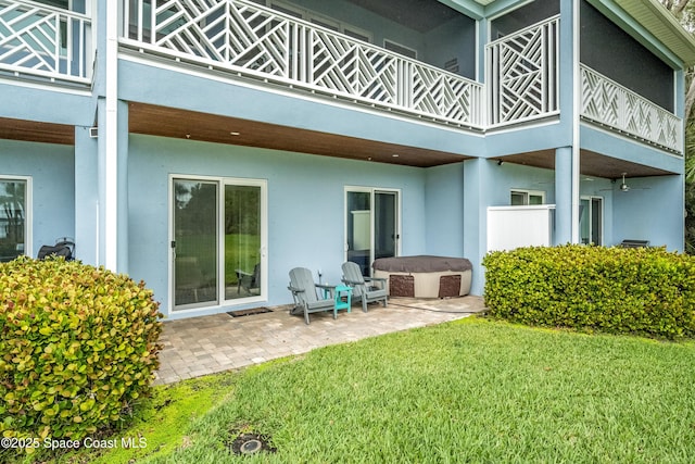 rear view of house with a lawn, a patio area, a balcony, and a hot tub