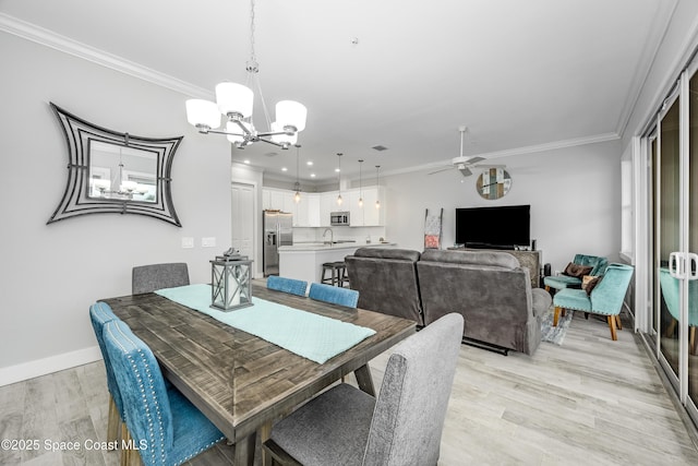 dining room featuring light wood-type flooring, ceiling fan with notable chandelier, ornamental molding, and sink