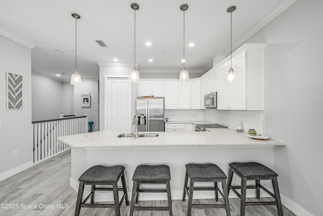 kitchen featuring kitchen peninsula, appliances with stainless steel finishes, decorative light fixtures, and white cabinetry