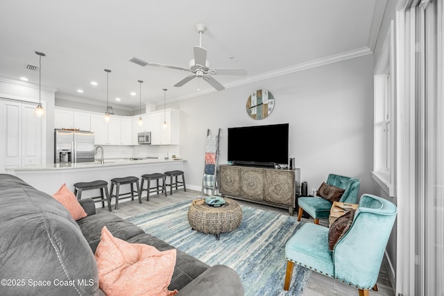 living room with light hardwood / wood-style flooring, ceiling fan, ornamental molding, and sink