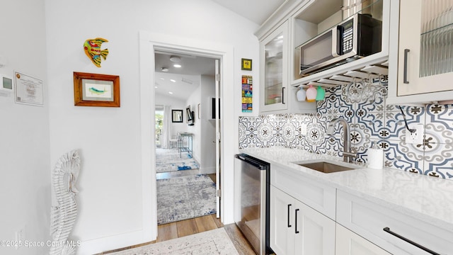 kitchen featuring light stone countertops, beverage cooler, sink, white cabinets, and lofted ceiling