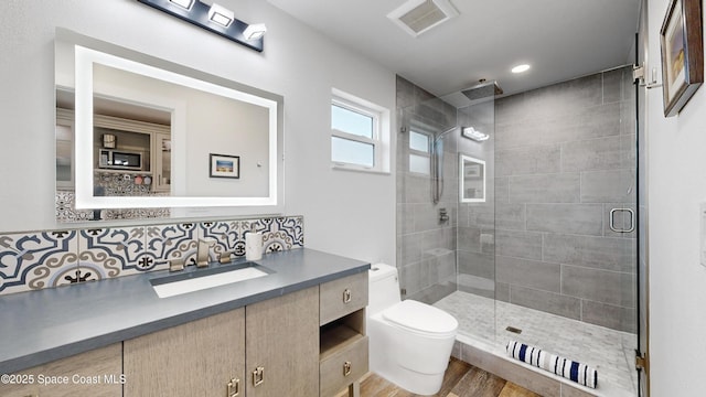 bathroom featuring tasteful backsplash, wood-type flooring, toilet, a shower with door, and vanity