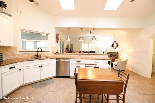 kitchen with a skylight, sink, stainless steel dishwasher, dark stone countertops, and pendant lighting