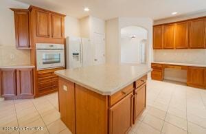 kitchen with a kitchen island, light tile patterned flooring, white appliances, and tasteful backsplash