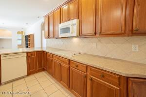 kitchen featuring kitchen peninsula, light tile patterned flooring, white appliances, and decorative backsplash