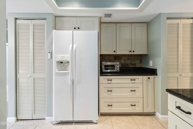 kitchen with light tile patterned floors, white refrigerator with ice dispenser, backsplash, and dark stone counters