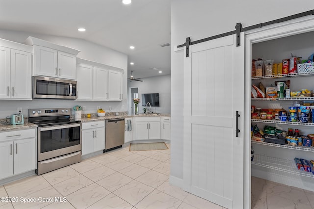 kitchen featuring white cabinets, appliances with stainless steel finishes, a barn door, and light stone counters