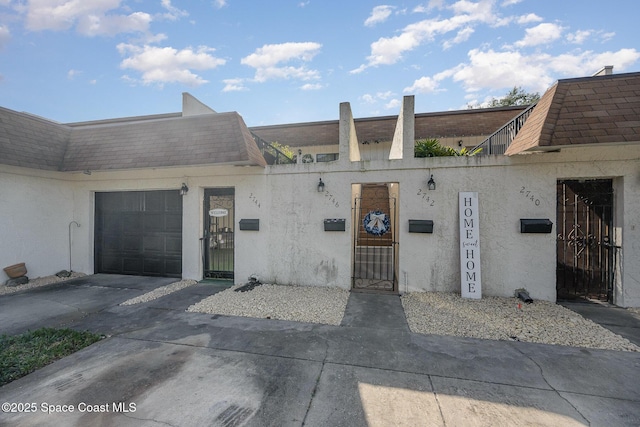 exterior space with a shingled roof, stucco siding, an attached garage, and mansard roof