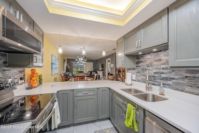 kitchen featuring pendant lighting, stainless steel appliances, gray cabinetry, a sink, and a peninsula