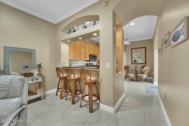 kitchen featuring tasteful backsplash, light tile patterned floors, a breakfast bar area, and ornamental molding