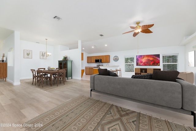 living room featuring vaulted ceiling, light hardwood / wood-style flooring, and ceiling fan with notable chandelier