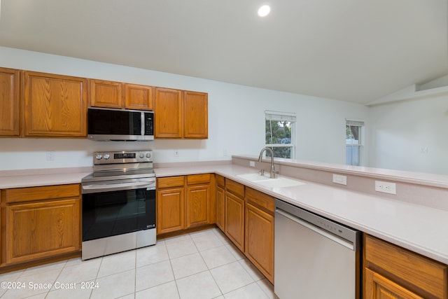 kitchen with lofted ceiling, sink, light tile patterned floors, appliances with stainless steel finishes, and kitchen peninsula