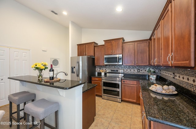 kitchen featuring light tile patterned floors, appliances with stainless steel finishes, decorative backsplash, a kitchen island with sink, and dark stone countertops