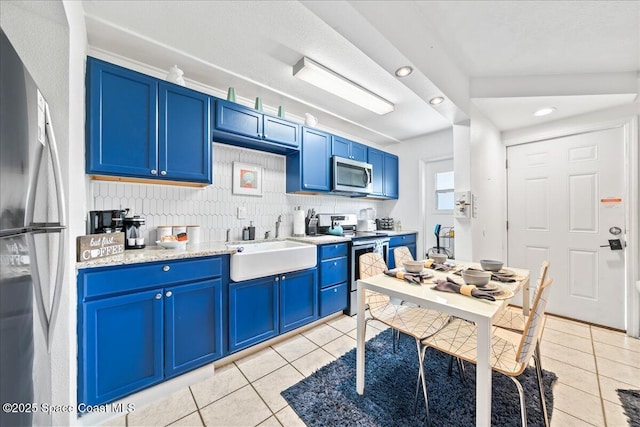 kitchen with light stone countertops, stainless steel appliances, sink, blue cabinetry, and light tile patterned flooring