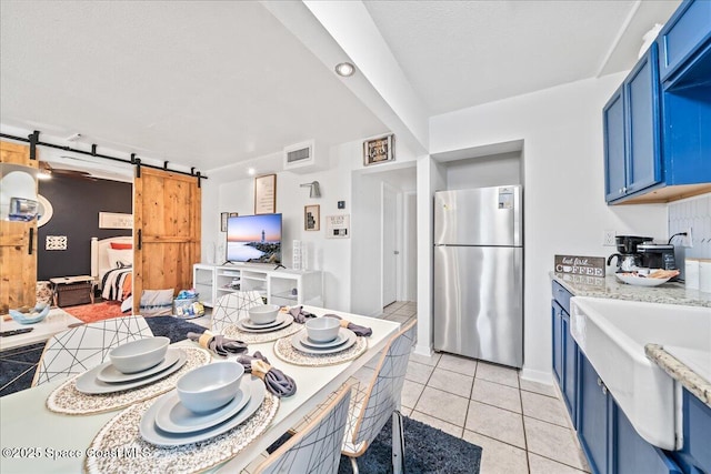 kitchen featuring stainless steel refrigerator, a barn door, blue cabinets, a textured ceiling, and light tile patterned floors