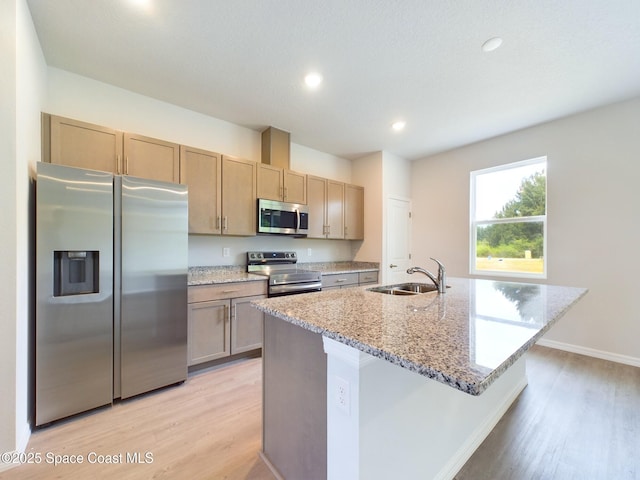 kitchen featuring light stone countertops, appliances with stainless steel finishes, sink, a center island with sink, and light hardwood / wood-style flooring